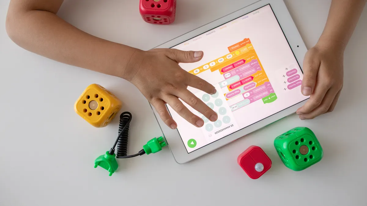 Tablet displaying colorful block coding with toy cubes